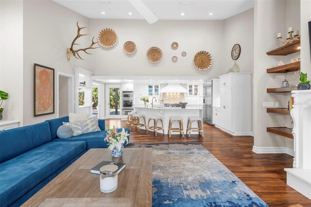 living room with sink, beamed ceiling, dark wood-type flooring, and a high ceiling