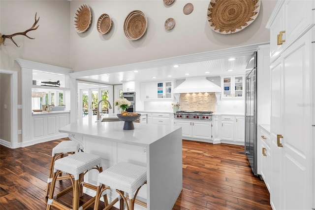 kitchen with premium range hood, stainless steel appliances, a center island with sink, white cabinets, and dark hardwood / wood-style floors