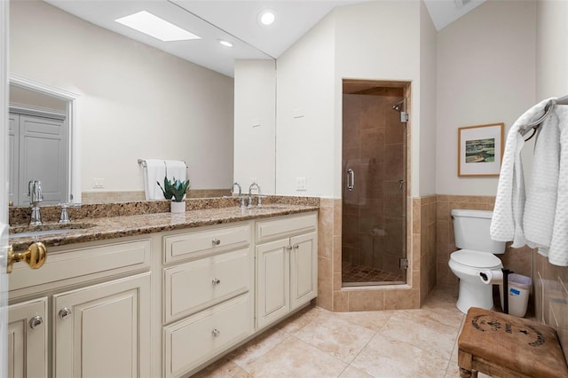 bathroom featuring tile patterned floors, toilet, a shower with door, vanity, and tile walls