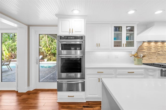 kitchen featuring white cabinetry, dark wood-type flooring, stainless steel appliances, decorative backsplash, and custom range hood