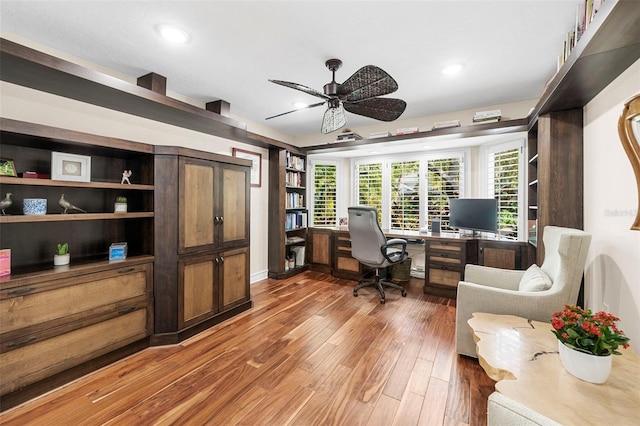 office area featuring wood-type flooring, built in desk, and ceiling fan