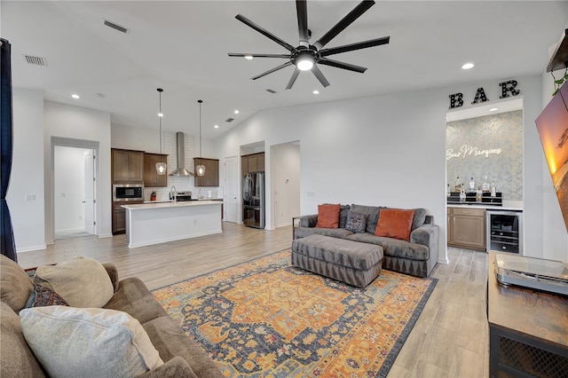 living room with wet bar, vaulted ceiling, ceiling fan, light wood-type flooring, and beverage cooler