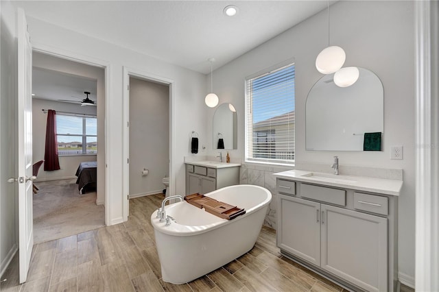 bathroom with hardwood / wood-style floors, a bathtub, vanity, ceiling fan, and toilet