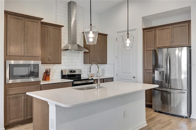 kitchen featuring sink, wall chimney range hood, pendant lighting, appliances with stainless steel finishes, and light wood-type flooring