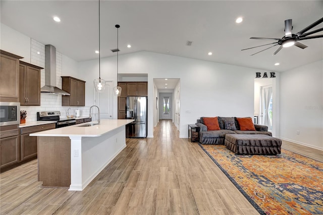 kitchen featuring sink, wall chimney range hood, light hardwood / wood-style flooring, vaulted ceiling, and appliances with stainless steel finishes