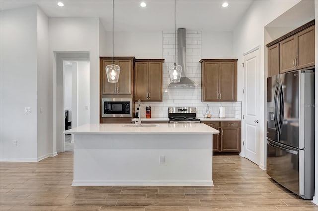 kitchen featuring appliances with stainless steel finishes, sink, wall chimney range hood, pendant lighting, and an island with sink