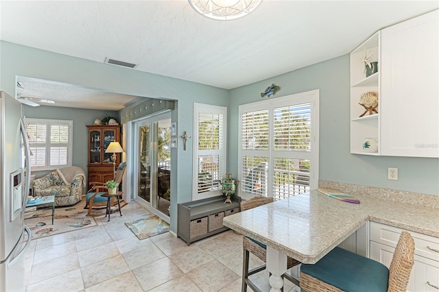 kitchen featuring a textured ceiling, light tile patterned floors, white cabinets, and stainless steel refrigerator with ice dispenser