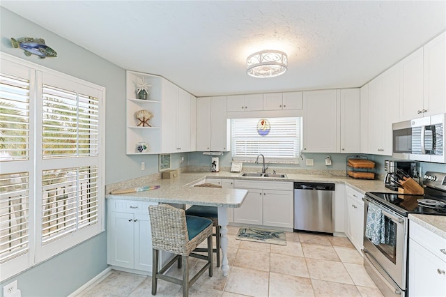 kitchen with a kitchen bar, stainless steel appliances, sink, light tile patterned floors, and white cabinets