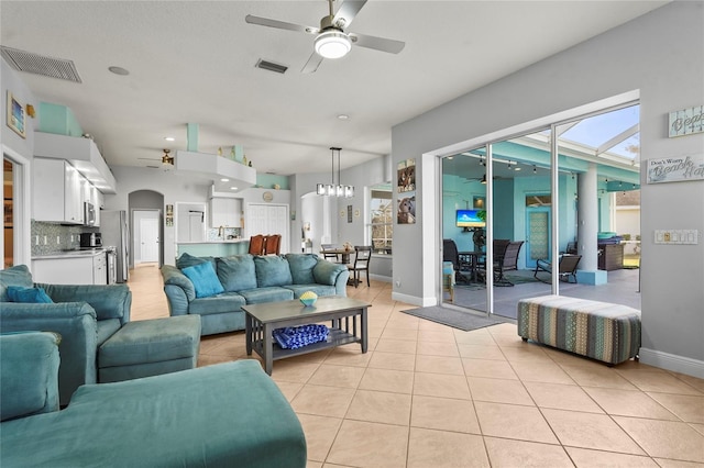 living room with light tile patterned floors, ceiling fan with notable chandelier, visible vents, and arched walkways