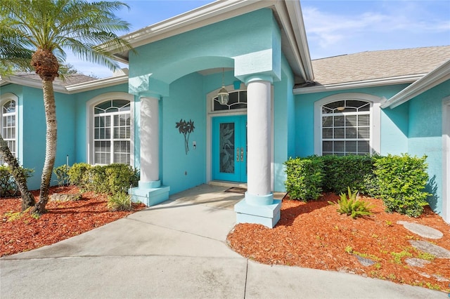 entrance to property featuring roof with shingles and stucco siding