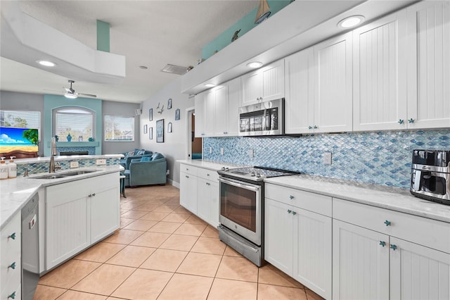 kitchen with light tile patterned flooring, a sink, appliances with stainless steel finishes, white cabinetry, and open floor plan