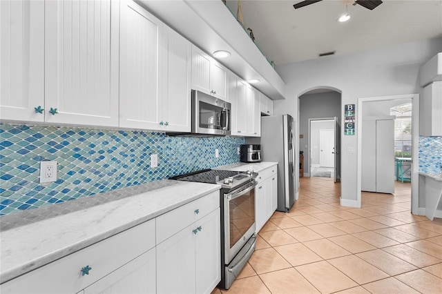 kitchen featuring tasteful backsplash, stainless steel appliances, arched walkways, white cabinets, and light tile patterned floors