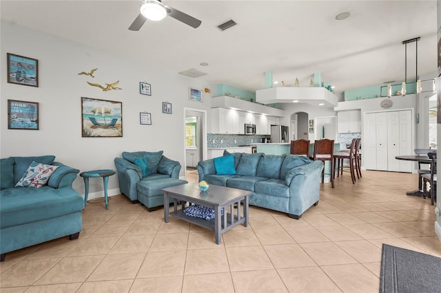 living room featuring light tile patterned floors, baseboards, visible vents, arched walkways, and ceiling fan