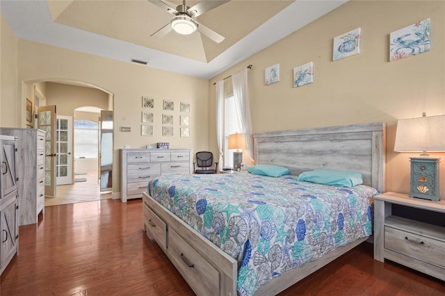 bedroom with visible vents, wood finished floors, arched walkways, a raised ceiling, and ceiling fan