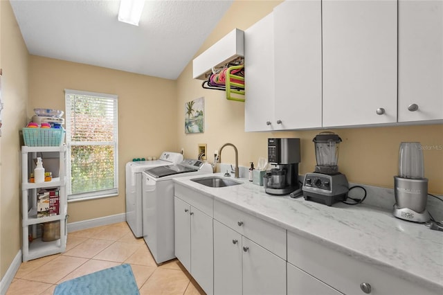 laundry area featuring a sink, cabinet space, light tile patterned floors, baseboards, and washing machine and clothes dryer