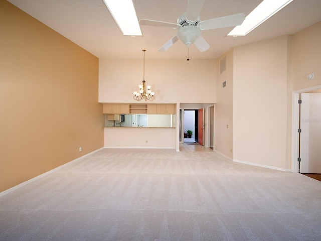 unfurnished living room with ceiling fan with notable chandelier, light colored carpet, and a high ceiling