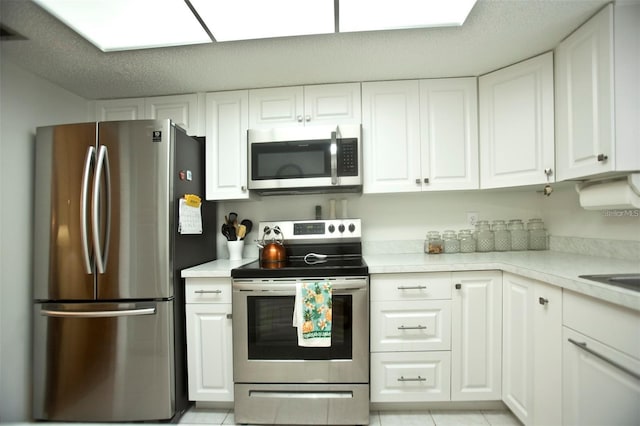 kitchen with white cabinets, appliances with stainless steel finishes, a textured ceiling, and light tile patterned floors