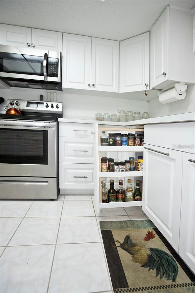 kitchen with a textured ceiling, light tile patterned flooring, white cabinetry, and stainless steel appliances