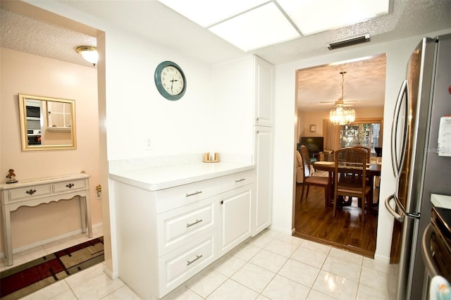 kitchen with stainless steel refrigerator, white cabinetry, light tile patterned floors, and pendant lighting