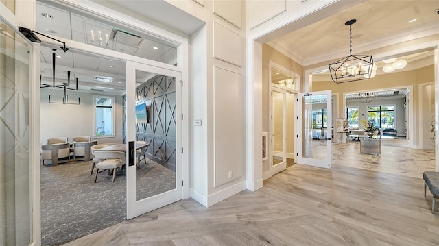 hall with french doors, light wood-type flooring, a notable chandelier, and ornamental molding