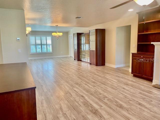 unfurnished living room with ceiling fan with notable chandelier, light hardwood / wood-style floors, and a textured ceiling