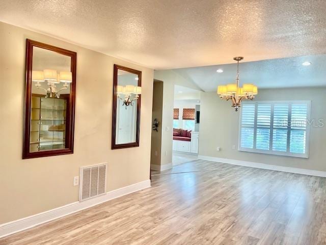 spare room featuring wood-type flooring, a textured ceiling, and a notable chandelier