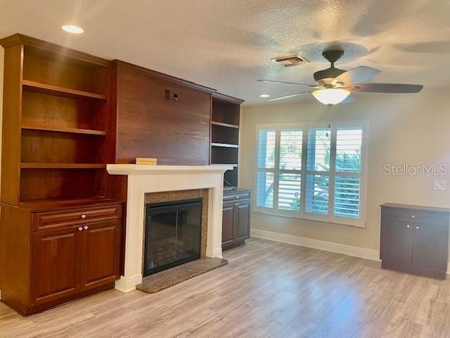 unfurnished living room with ceiling fan, light wood-type flooring, and a textured ceiling