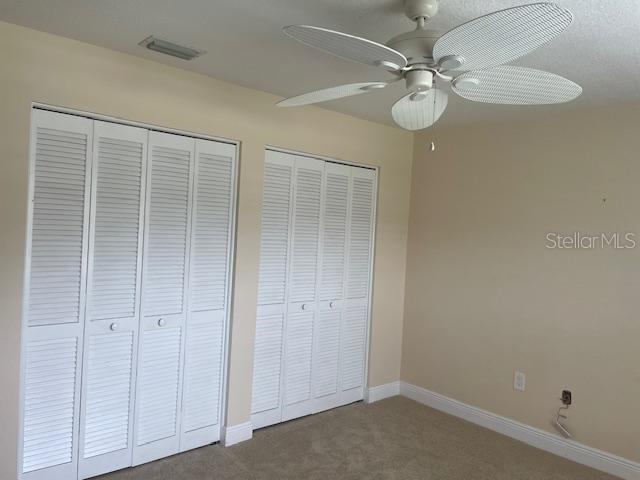 unfurnished bedroom featuring carpet, ceiling fan, and multiple closets