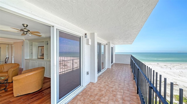 balcony featuring ceiling fan, a water view, and a view of the beach