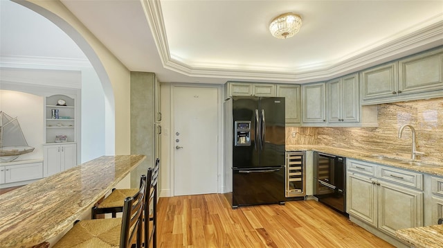 kitchen featuring light stone counters, black fridge with ice dispenser, light hardwood / wood-style floors, and sink