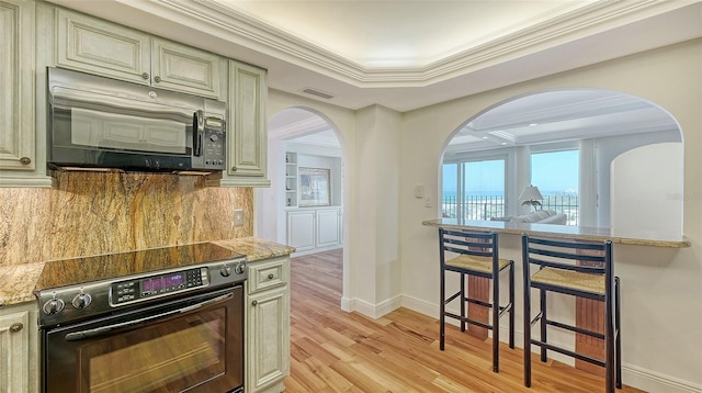 kitchen featuring light stone countertops, tasteful backsplash, black electric range oven, cream cabinets, and light hardwood / wood-style floors