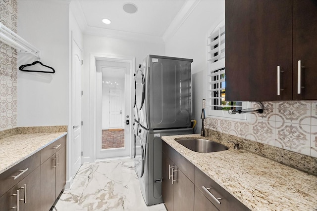 laundry room with cabinets, stacked washing maching and dryer, sink, and ornamental molding