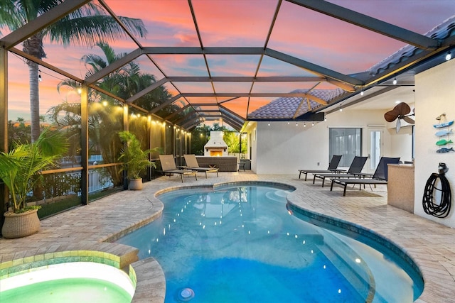 pool at dusk featuring an outdoor fireplace, glass enclosure, and a patio area