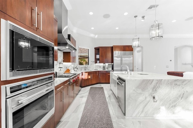 kitchen featuring pendant lighting, wall chimney range hood, built in appliances, light stone counters, and a large island with sink