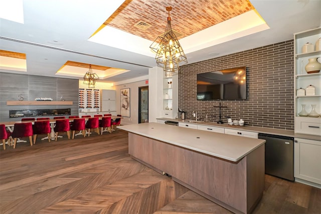 kitchen with a raised ceiling, dishwasher, a kitchen island, and decorative light fixtures