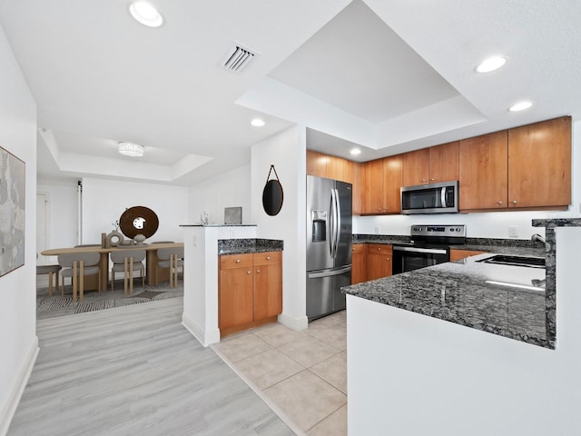 kitchen with light wood-type flooring, kitchen peninsula, stainless steel appliances, and a tray ceiling