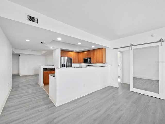 kitchen with light wood-type flooring, a barn door, stainless steel appliances, and kitchen peninsula