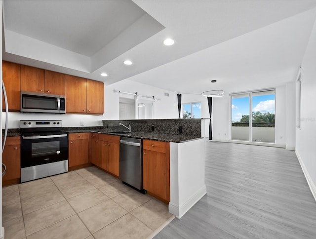 kitchen featuring dark stone counters, sink, light wood-type flooring, appliances with stainless steel finishes, and kitchen peninsula