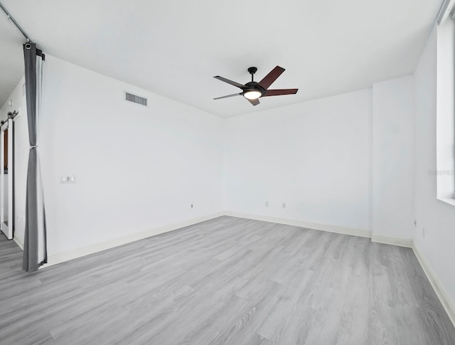 spare room with ceiling fan, a barn door, and light hardwood / wood-style flooring