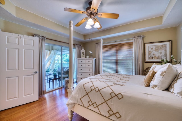 bedroom featuring ceiling fan, access to exterior, light hardwood / wood-style flooring, and a tray ceiling