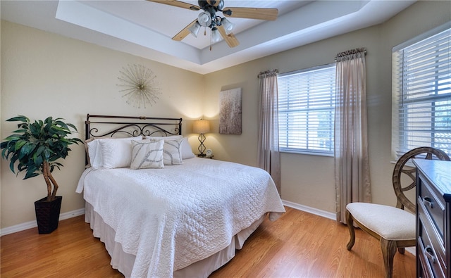 bedroom with ceiling fan, light hardwood / wood-style floors, and a tray ceiling