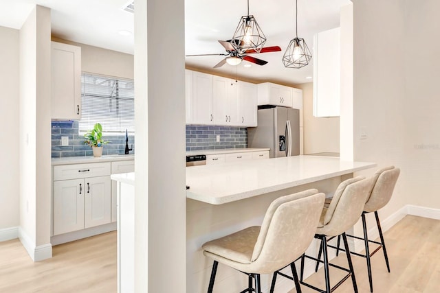 kitchen featuring white cabinetry, a kitchen bar, stainless steel fridge with ice dispenser, and hanging light fixtures