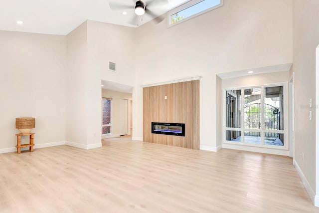 unfurnished living room with a fireplace, ceiling fan, light hardwood / wood-style flooring, and a high ceiling