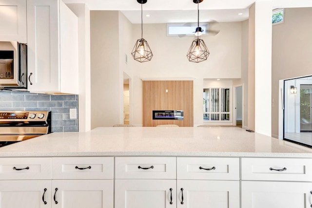 kitchen with light stone countertops, appliances with stainless steel finishes, decorative light fixtures, and white cabinetry