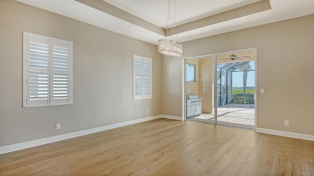 unfurnished room featuring an inviting chandelier, light hardwood / wood-style floors, and a raised ceiling