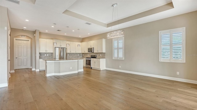 kitchen featuring pendant lighting, a center island, light hardwood / wood-style flooring, appliances with stainless steel finishes, and a tray ceiling