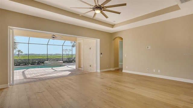 spare room featuring a tray ceiling, ceiling fan, and light wood-type flooring