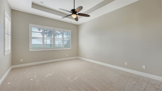 spare room with a raised ceiling, ceiling fan, and light carpet