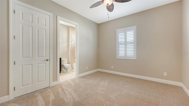 unfurnished bedroom featuring ceiling fan, light colored carpet, and ensuite bath