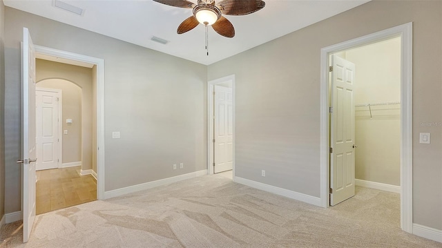 bedroom featuring a closet, a walk in closet, light colored carpet, and ceiling fan